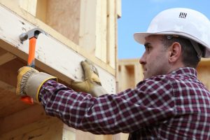 Worker nailing wooden framed house