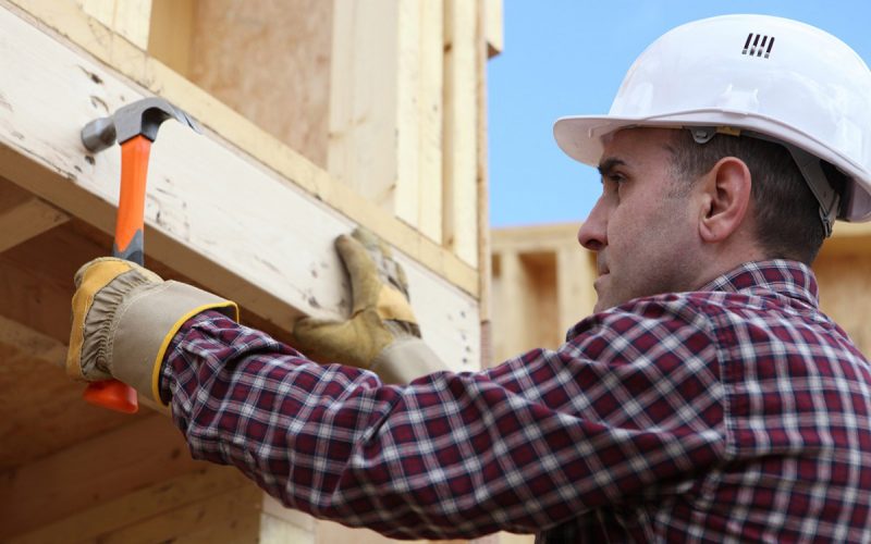 Worker nailing wooden framed house